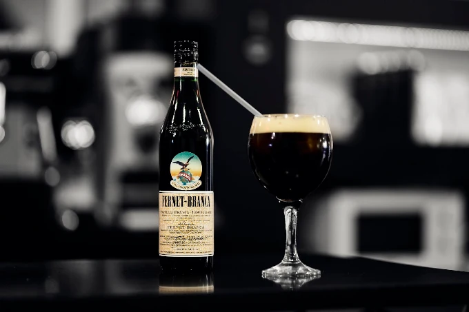 Botella de Fernet-Branca junto a una copa de fernet con coca