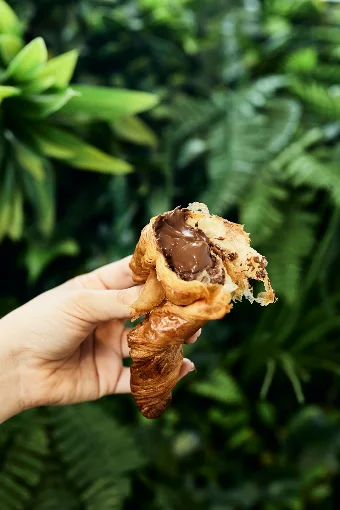 Mano sosteniendo una medialuna abierta rellena de chocolate