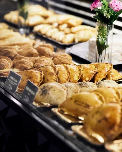Vitrina del café con bandejas de empanadas, medialunas y facturas